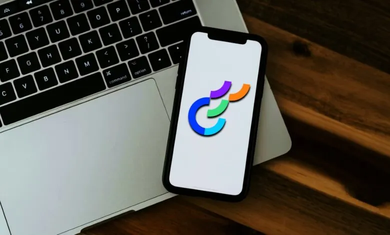 Optimizely logo on phone atop laptop, wooden desk background.