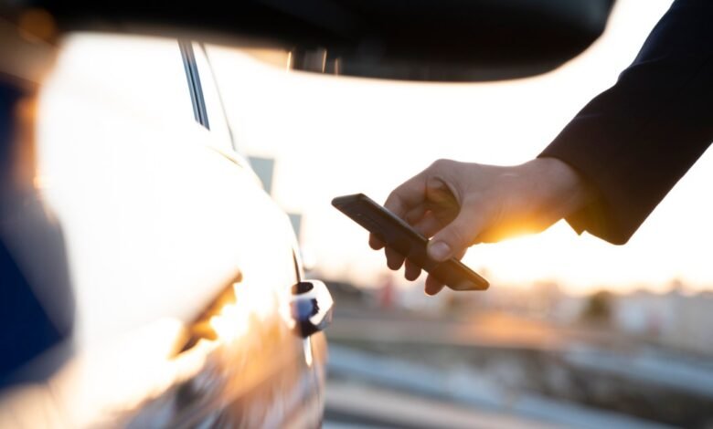 Person unlocking car door with smartphone, sunset background.