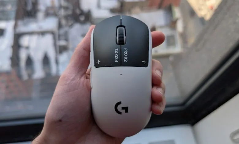 Hand holding a Logitech PRO X SUPERLIGHT 2 gaming mouse, white and black.