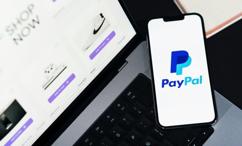 PayPal logo on phone next to laptop showing online shopping site.