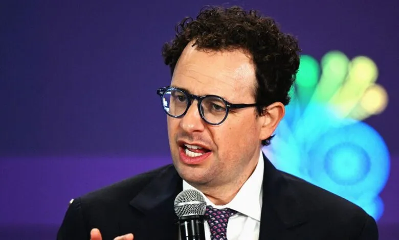 Man with curly hair and glasses speaking into a microphone.