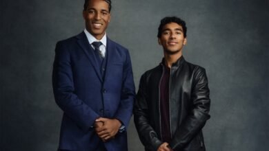 Two young men stand side-by-side against a gray backdrop.