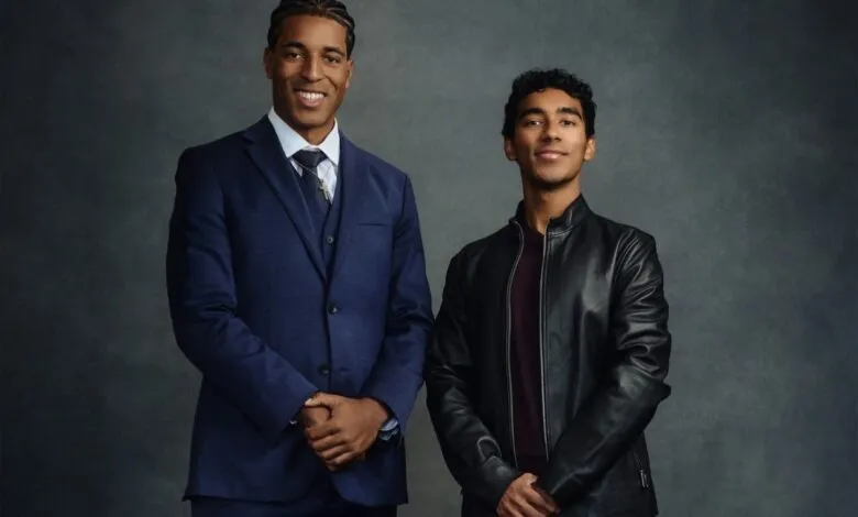 Two young men stand side-by-side against a gray backdrop.