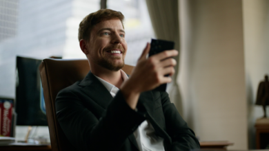 Man in suit smiles while holding phone in office setting.