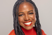 Close-up portrait of a smiling Black woman with dreadlocks and red lipstick.
