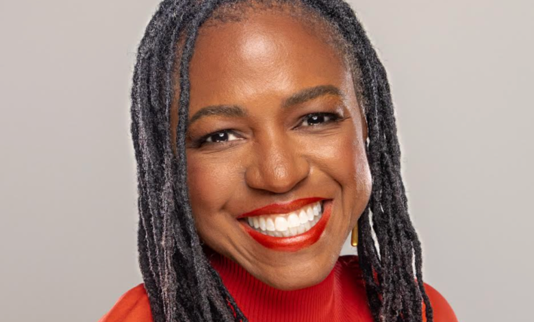 Close-up portrait of a smiling Black woman with dreadlocks and red lipstick.
