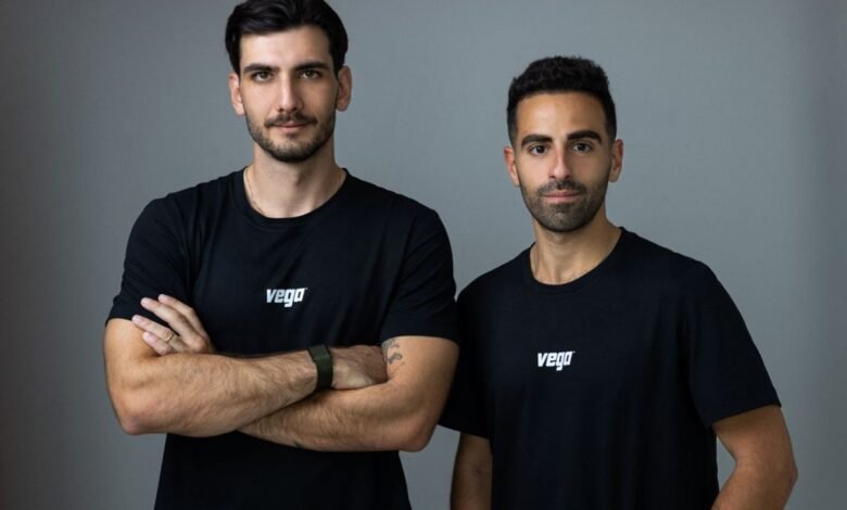 Two men in black Vega t-shirts pose against a gray backdrop.