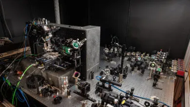Complex optical setup with lasers, lenses, and mirrors on a metal breadboard.