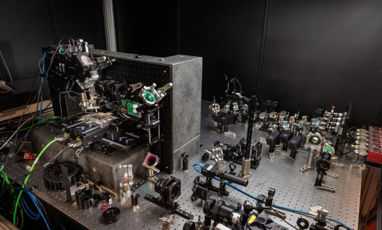 Complex optical setup with lasers, lenses, and mirrors on a metal breadboard.