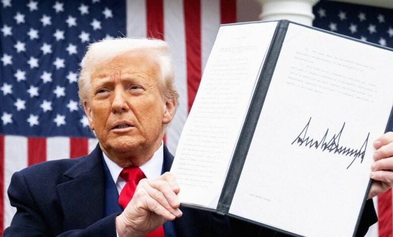 Donald Trump holds signed document against American flag backdrop.