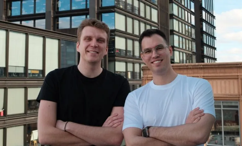 Two men stand smiling with arms crossed against a modern building backdrop.
