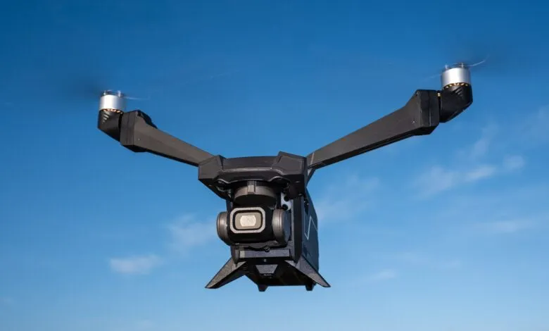 Black drone with camera flying against a clear blue sky.
