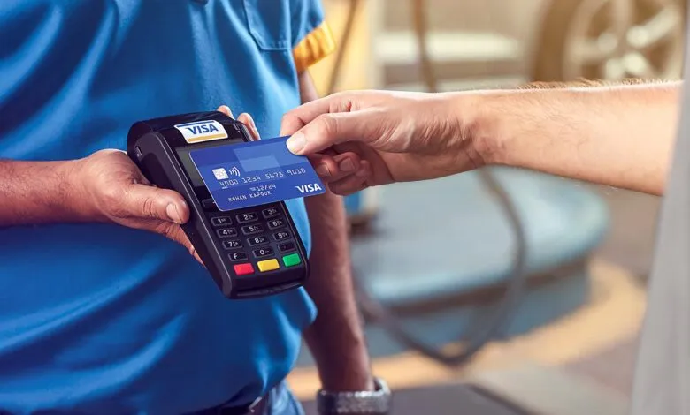 Person paying with a blue VISA credit card at a payment terminal.