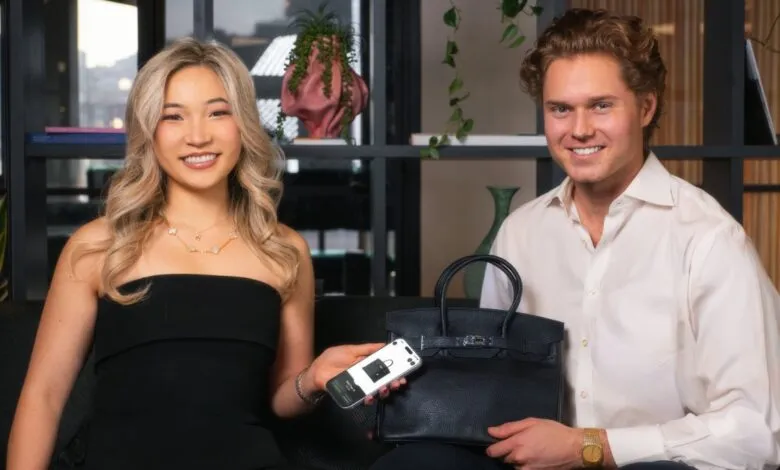 Two smiling people pose with a black handbag and phone showing a handbag image.