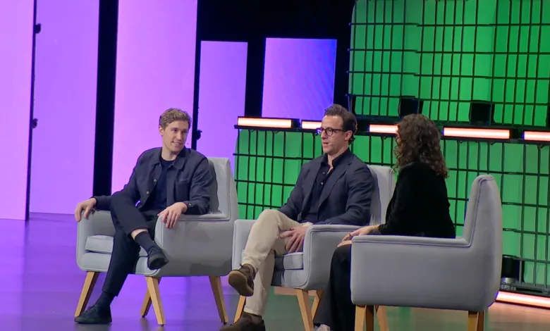 Three people sit in chairs on stage at a conference, facing the audience.