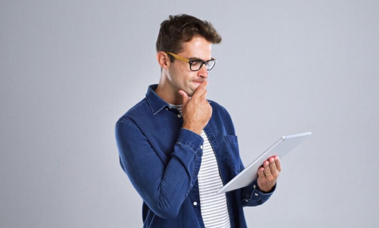 Man with glasses thoughtfully uses a tablet device.