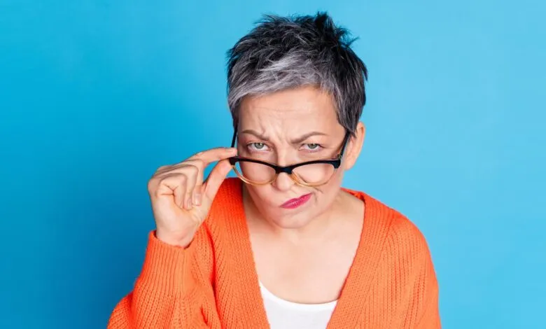 Woman with glasses raised, looking skeptical against a blue background.