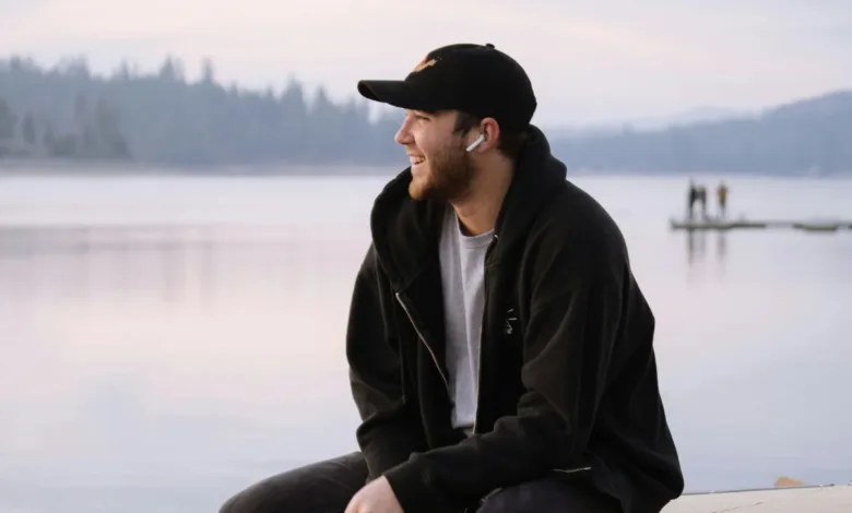 Young man with AirPods sitting by a lake, looking off to the side.