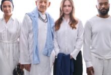 Four people stand together in white clothing against a bright white background.