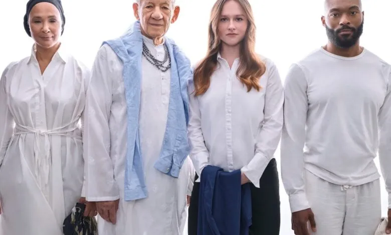 Four people stand together in white clothing against a bright white background.