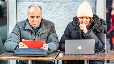 Man with iPad and woman with MacBook working at outdoor cafe.