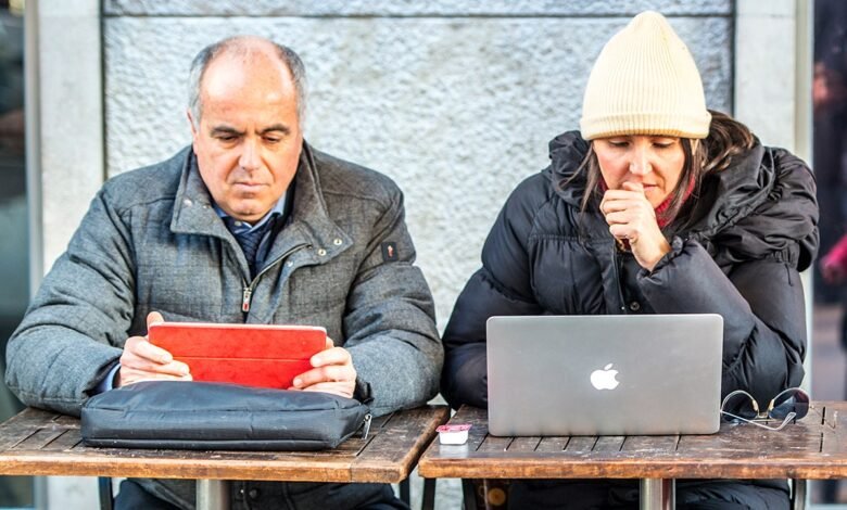 Man with iPad and woman with MacBook working at outdoor cafe.