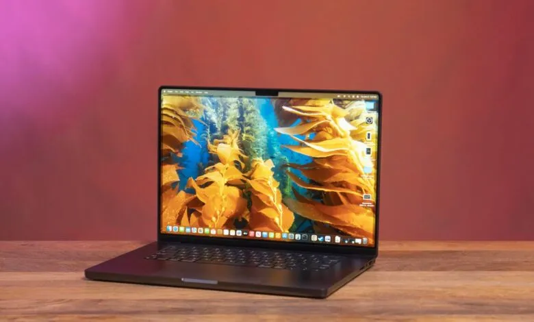Open 16-inch MacBook Pro on a wooden surface with a kelp forest wallpaper.