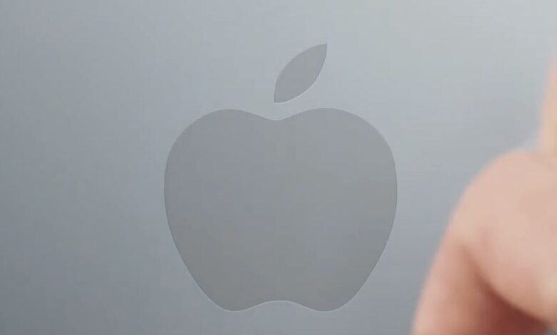 Apple logo on a gray surface with a blurred finger in the foreground.