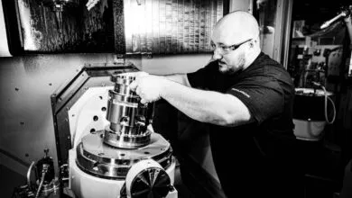 Man in safety glasses loads metal part into CNC machine.