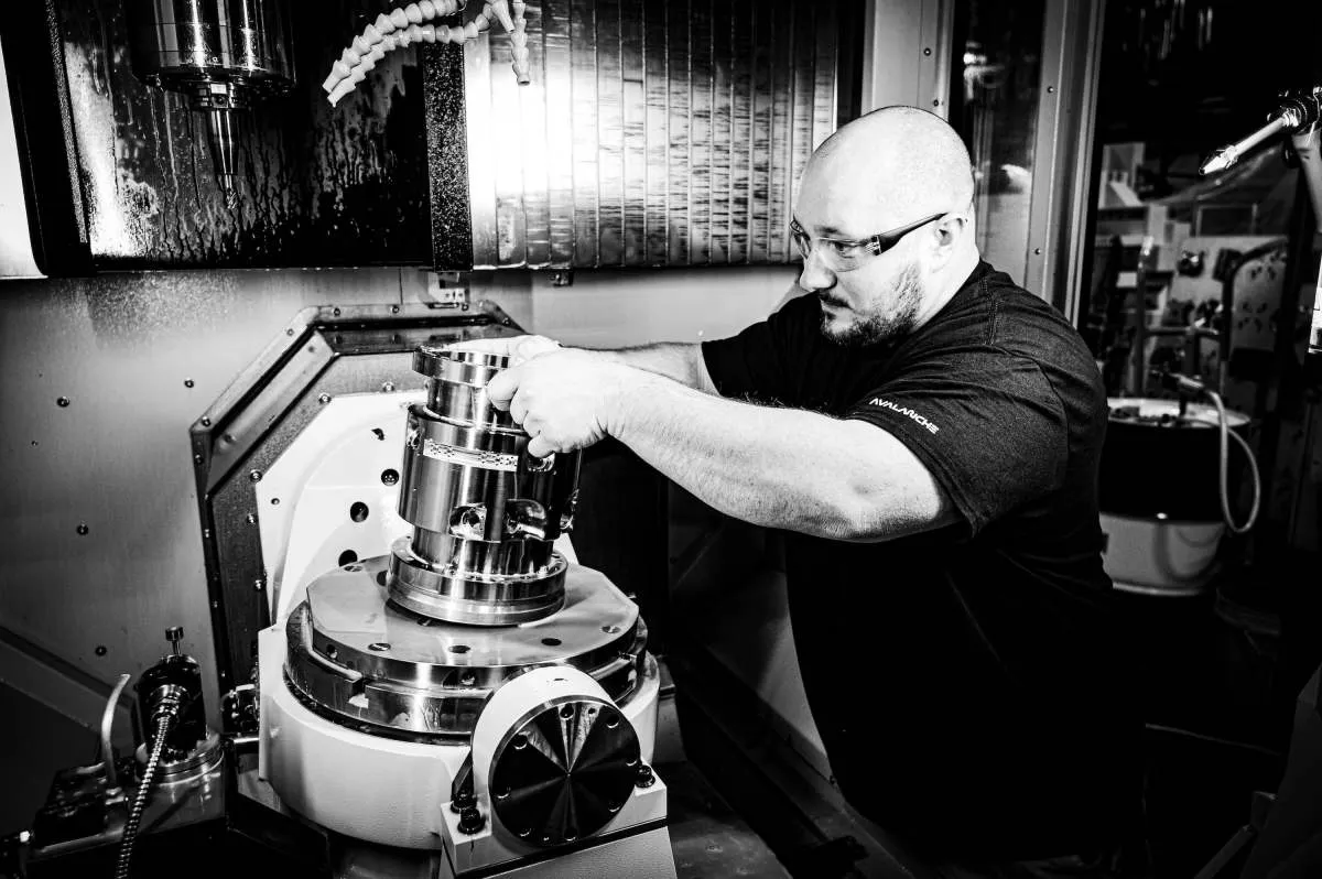 Man in safety glasses loads metal part into CNC machine.