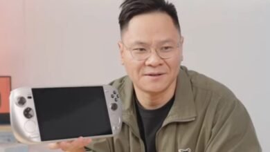 Man holds silver handheld gaming device with blank screen, smiling at the camera.