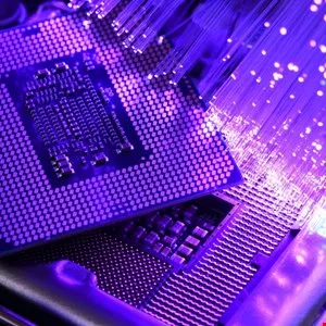 Close-up of computer chips and fiber optic cables, illuminated in purple light.