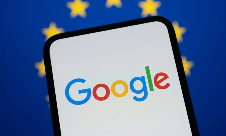 Smartphone displays Google logo against blurred EU flag backdrop.