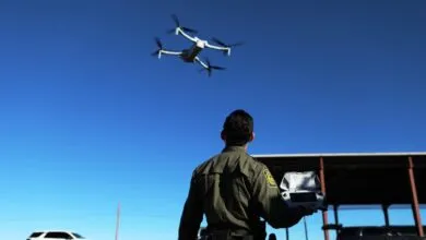 Border Patrol agent operates drone against clear blue sky.