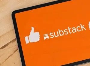 Tablet displaying the Substack logo with a thumbs up icon on an orange screen.