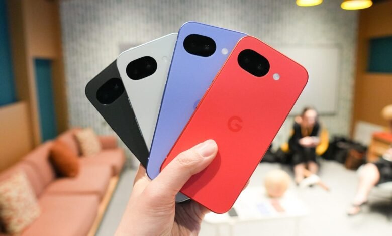 Hand holding four colorful Google Pixel 8a phones: black, white, blue, and red.