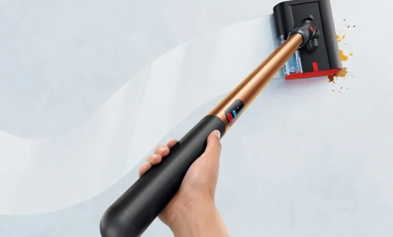 Person cleans wall with Dyson WashG1, removing stains.