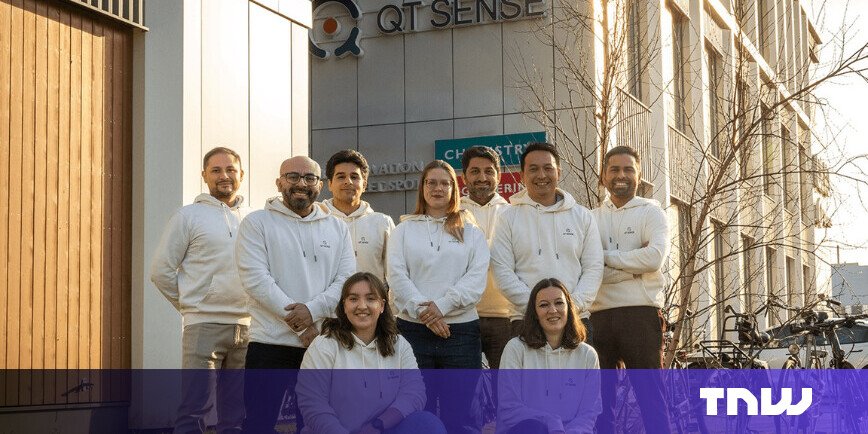 Group of nine people in matching hoodies posing in front of the QT Sense building.