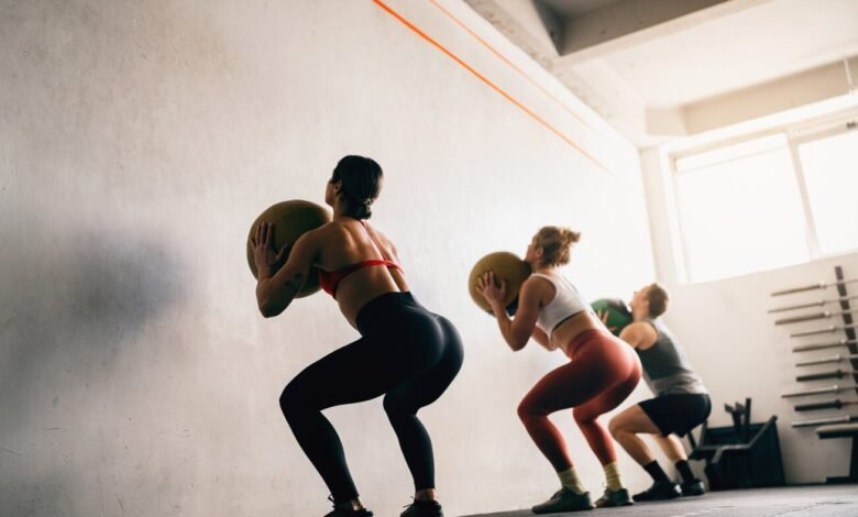 Three people doing wall ball squats in a bright gym setting.