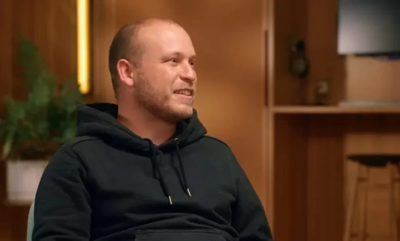 Man with short hair and black hoodie smiles in a warm, inviting room.