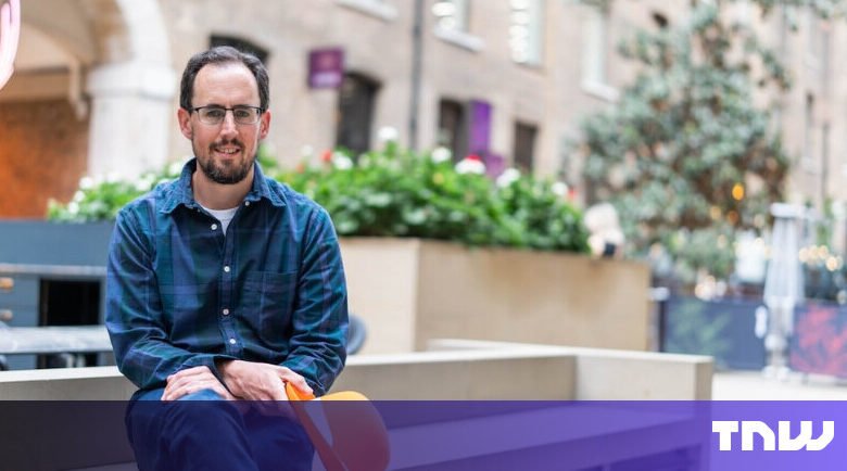 Man with glasses sits outdoors in a blue plaid shirt.