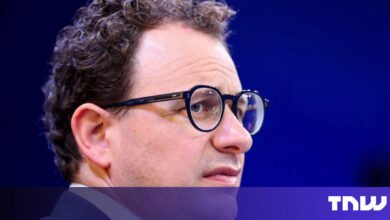 Close-up of man with glasses against a blue backdrop.