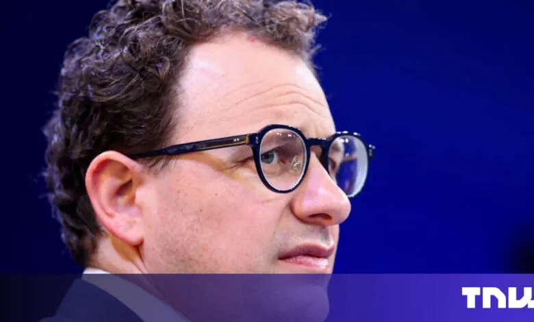 Close-up of man with glasses against a blue backdrop.