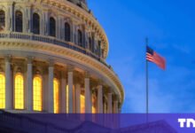 US Capitol Building dome with illuminated windows and waving American flag.