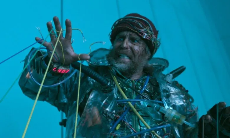 Distressed man entangled in wires, wearing a makeshift tech suit.