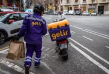 Getir delivery person walking with bags next to scooter.