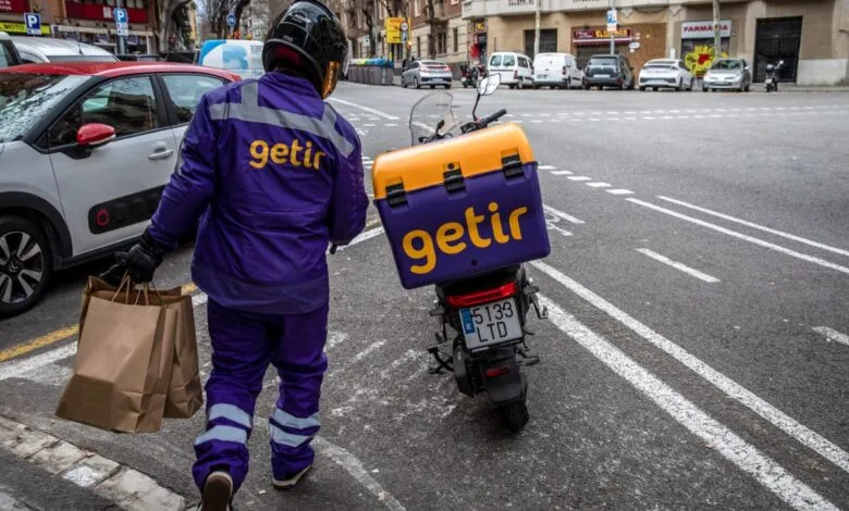 Getir delivery person walking with bags next to scooter.