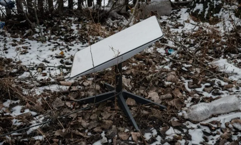 Starlink satellite dish sits among snow and debris outdoors.