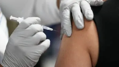 Close-up of gloved hand administering vaccine into a person's arm.