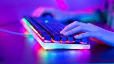 Hands type on a backlit gaming keyboard with vibrant RGB lighting.